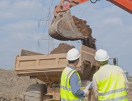 Hispanic construction workers watching dirt falling into dump truck