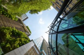 Low angle shot of modern glass buildings and green with clear sky background.